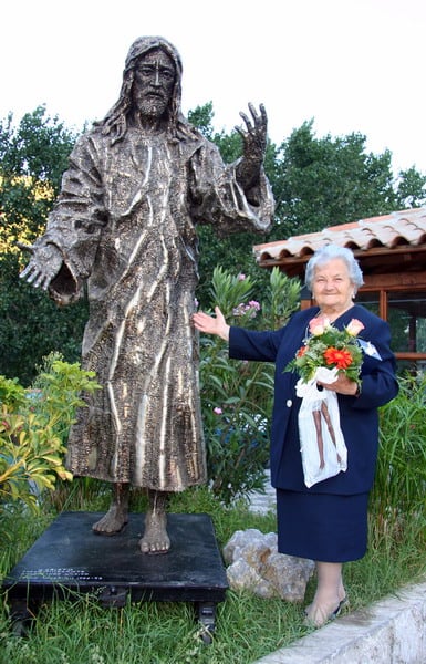 Una fedele in posa accanto a una scultura sacra di Nino Ucchino