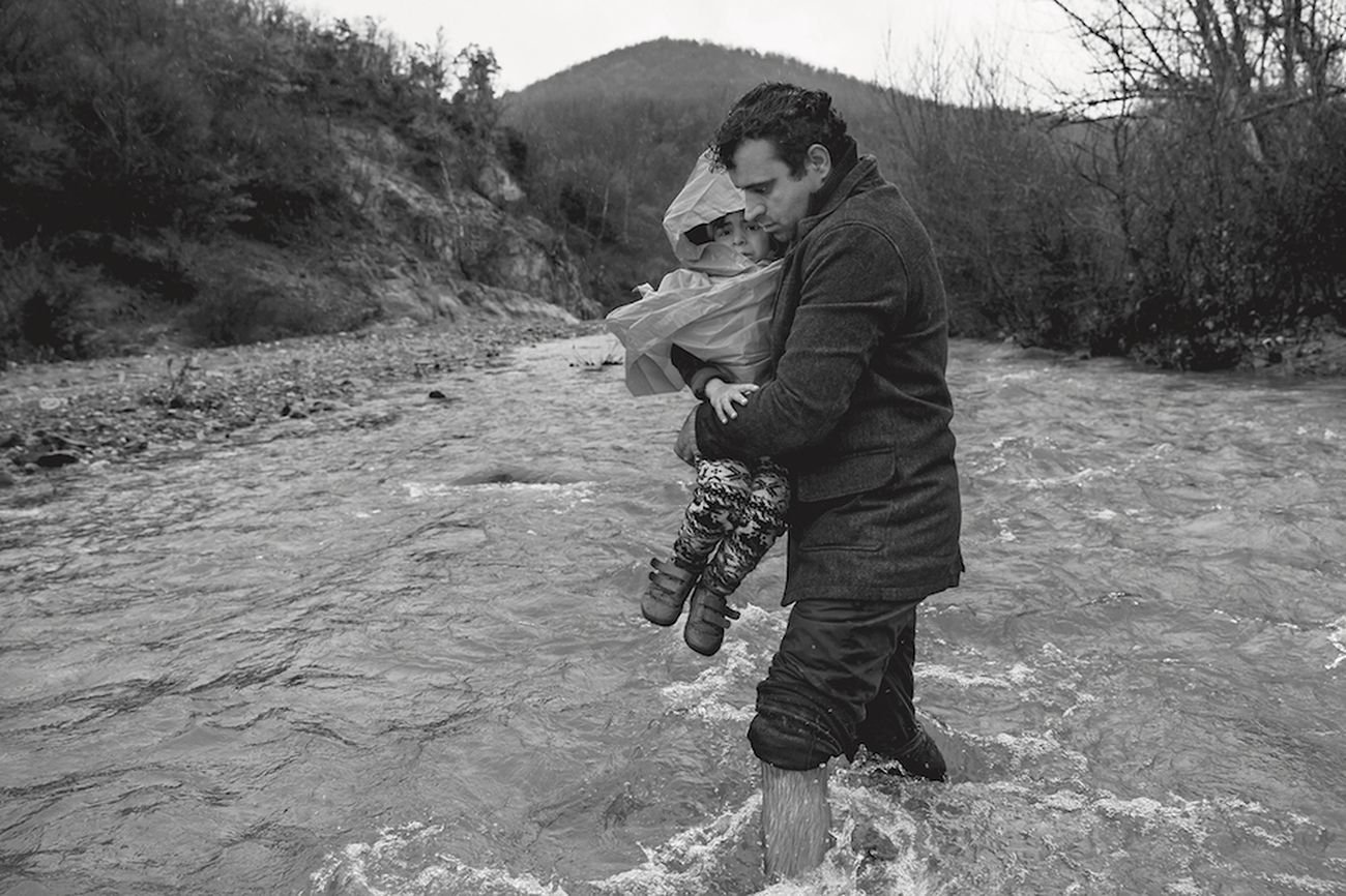 Un uomo porta in braccio il figlio mentre tenta di attraversare il confine con la Macedonia. Macedonia, 2016 © James Nachtwey/Contrasto