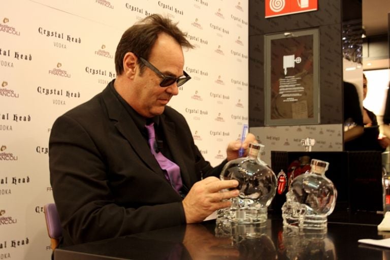 Autografo su bottiglia foto Michela Deponti Dan Aykroyd distillatore a Milano: bottiglia d’artista e design italiano per Crystal Head, vodka con cui l’ex Blues Brother ha conquistato il mondo. Partendo dal suo Canada per spopolare persino a Mosca