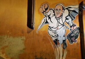 Cancellato lo sticker di Mauro Pallotta col Papa-Superman a Roma. Sebbene fosse piaciuto al Vaticano. Divampa la polemica (anche politica) e l’artista annuncia altri interventi