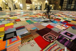 Giornata internazionale contro la violenza sulle donne. A Brescia un’immensa coperta handmade srotolata in Piazza Vittoria. Simboli, rituali, sensibilità collettive