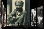 Nello schermo centrale una fotografia di Gustav Klimt che bene rappresenta il carattere eccentrico dell’artista. Sugli schermi laterali foto di gruppo dei secessionisti viennesi
