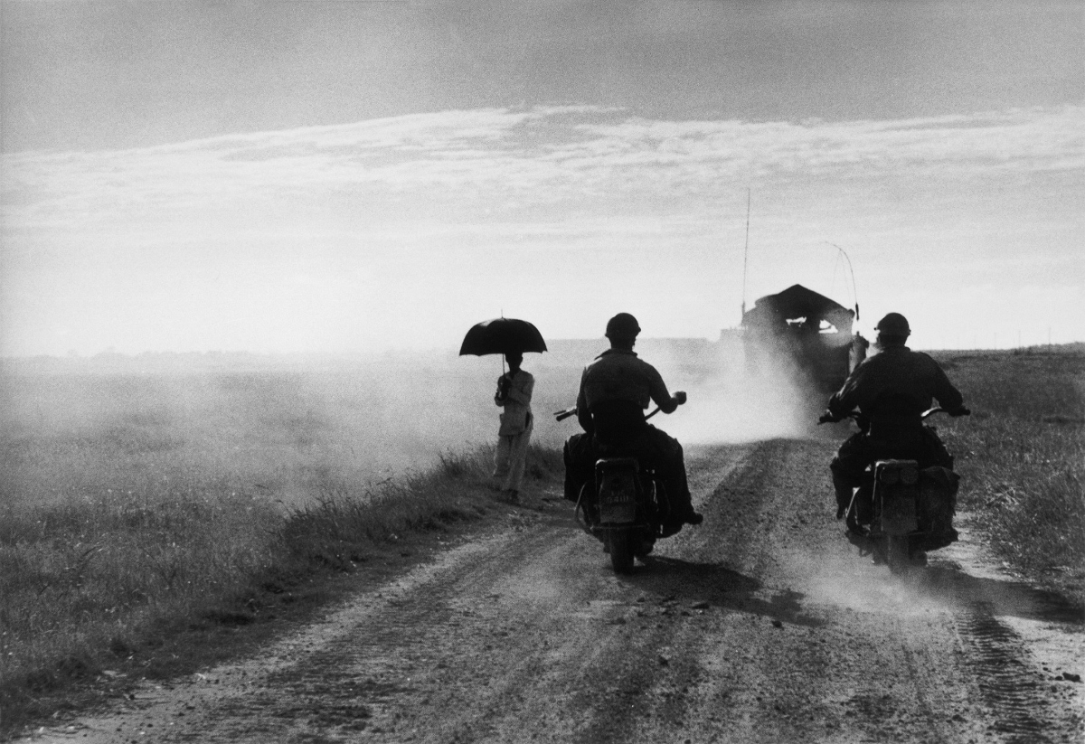 Motorcyclists and woman walking on the road from Nam Dinh to Thai Binh, Vietnam, May 25, 1954 © Robert Capa © International Center of PhotographyMagnum Photos