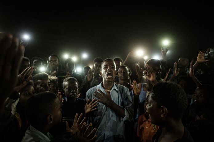 People chant slogans as a young man recites a poem, illuminated by mobile phones, before the opposition's direct dialog with people in Khartoum on June 19, 2019. - People chanted slogans including 