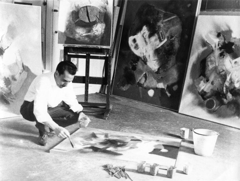 Edmondo Bacci nello studio, Venezia, 1961. Sul cavalletto, Senza titolo (1957 c.), proseguendo verso destra, Avvenimento #316 (Omaggio a Gagarin) (1958), Avvenimento #328 (1959 c.). Archivio Edmondo Bacci, Venezia