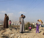 Ivor Prickett. Rifugiati siriani che vivono a Fayda, insediamento di tende nella valle della Beqaa in Libano, stanno fuori dalle baracche dove vivono, di fianco a un canale di acqua inquinata. Fotografia dalla serie "End of the Caliphate". Courtesy and © Ivor Prickett