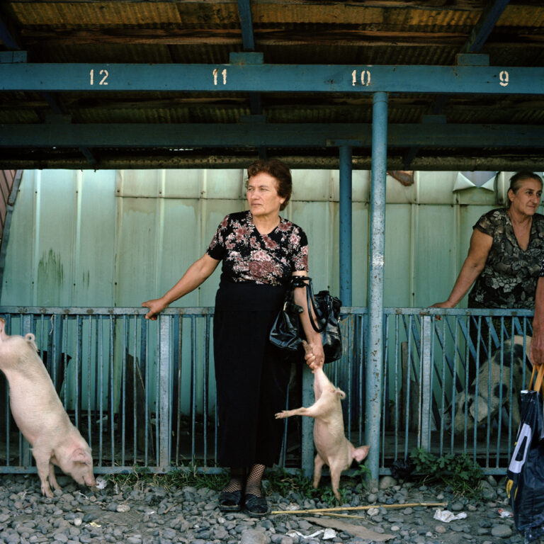 Ivor Prickett. Una donna georgiana mingreliana aspetta di vendere un maialino al mercato di Gali. 2010, Gali, Abkhazia. Fotografia dalla serie "Returning Home - Abkhazia". Courtesy and © Ivor Prickett