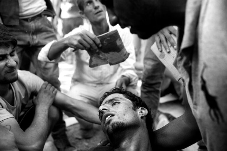 Stanchezza e lunghe ore di attesa nel caldo cocente provocano il collasso e lo svenimento dei rifugiati sull'isola di Lesbo, Grecia, 2016 © Paolo Pellegrin / Magnum Photos