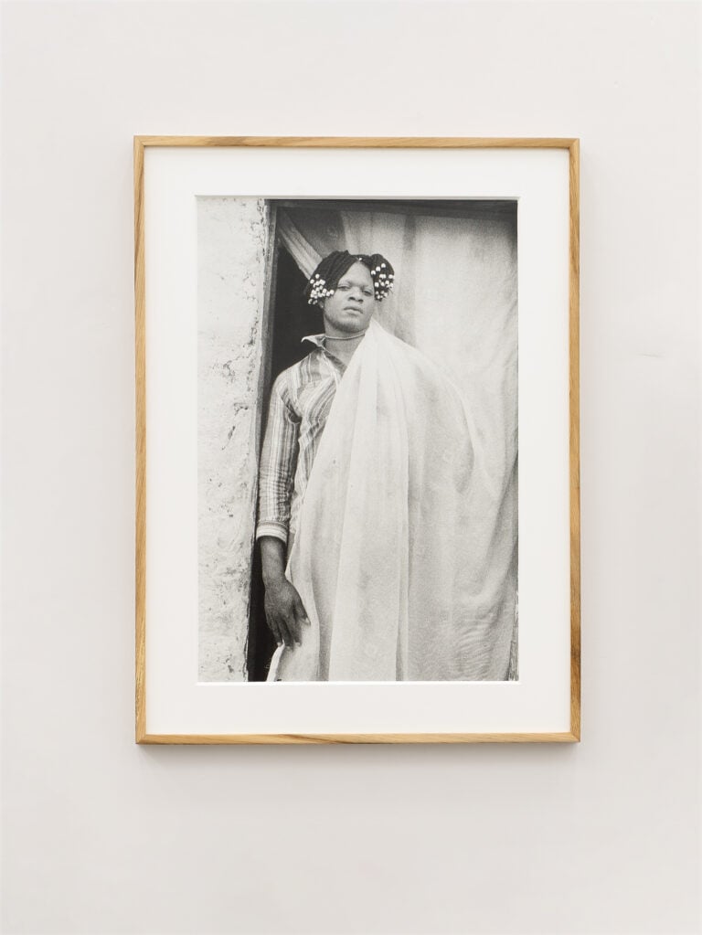 Sabelo Mlangeni, Jenine wrapped with door curtain at the door of her house and friends, Kigoma, Lubumbashi, 2017. Courtesy ADA Project, Roma